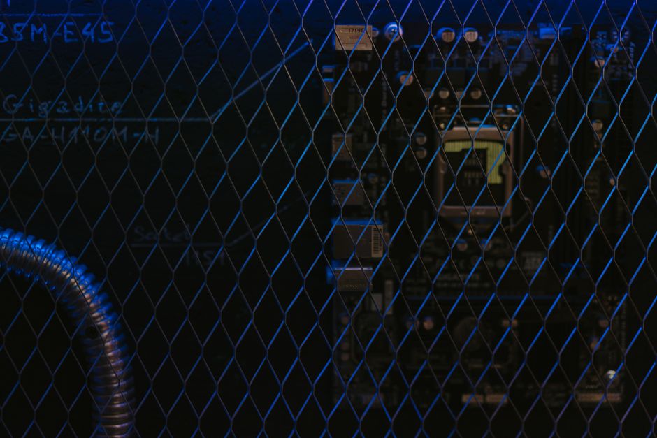 Artistic view of a circuit board through metal mesh with blue lighting.