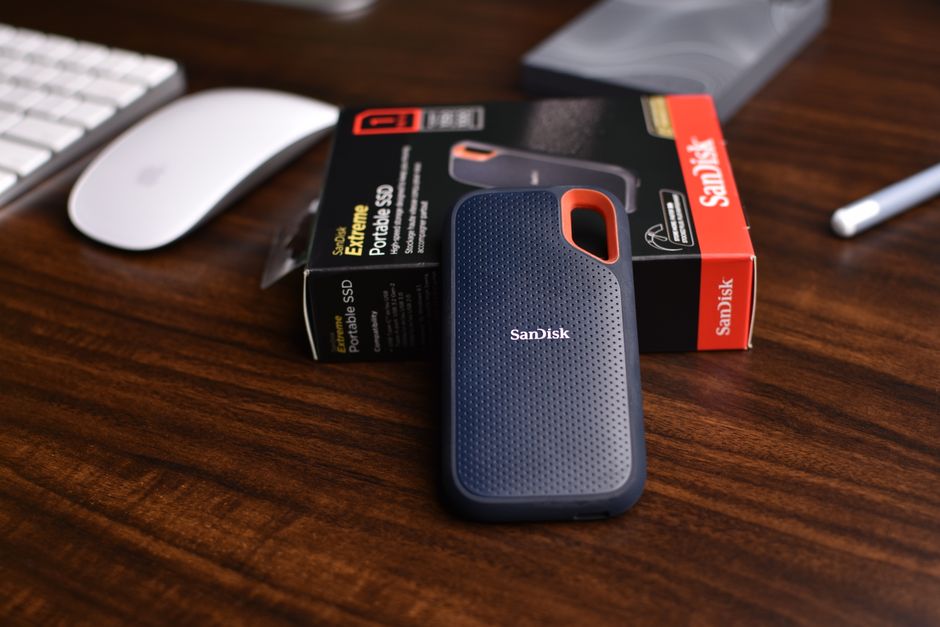 Close-up of a SanDisk portable SSD with a box and mouse on a wooden desk, ideal for tech-related themes.