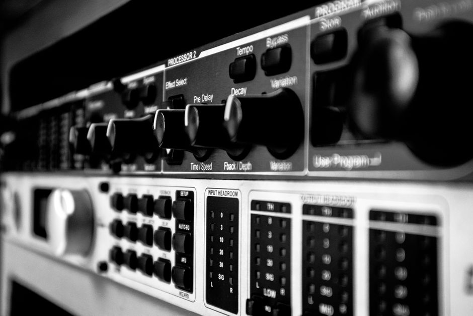 Detailed black and white close-up of an audio mixer highlighting various control knobs and switches.