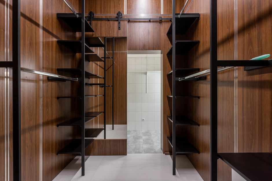 Empty black shelves and racks placed in modern walk in closet with brown walls and mirror with reflection at home