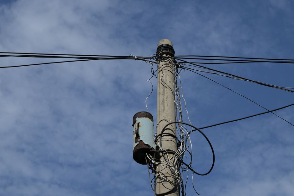 Photograph of a utility pole and power lines under a bright blue sky with scattered clouds.