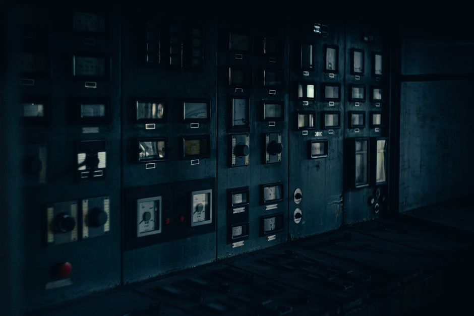 A dark, retro industrial control panel with dials and gauges in a maintenance room.