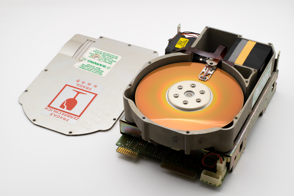 Close-up of an open vintage hard disk drive showing internal components and caution labels.
